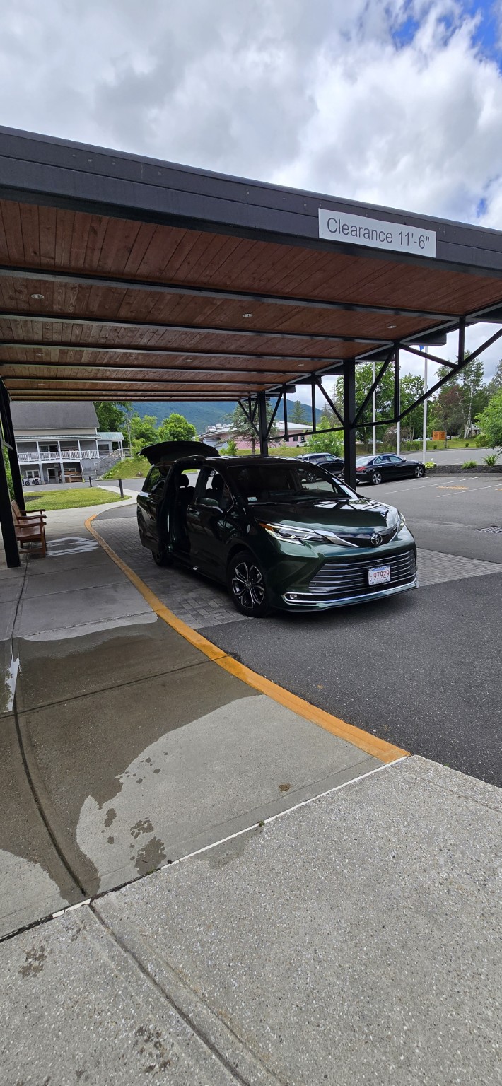 A clean, forest green van sits curbside of a building with its side door and 